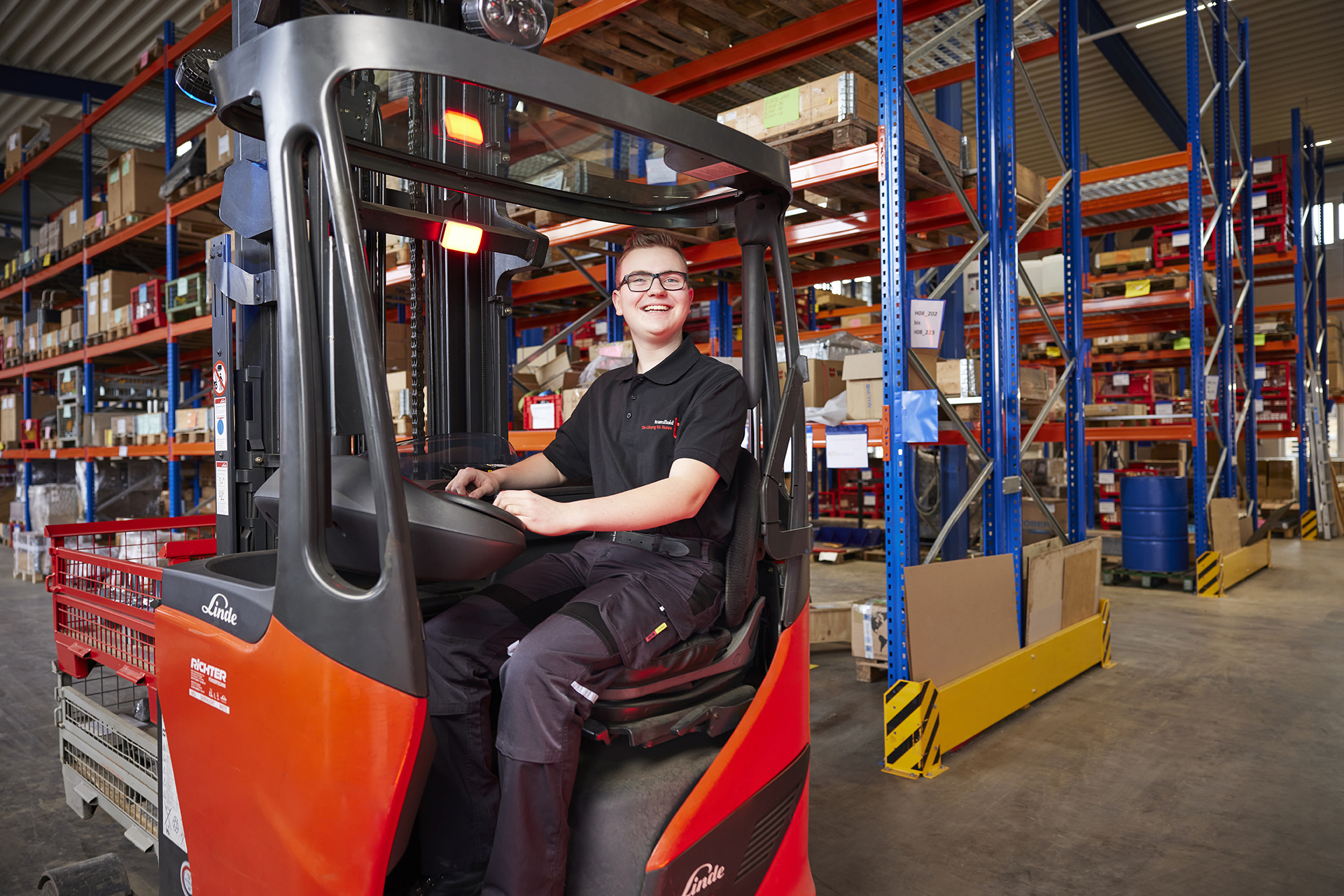 Auszubildender Fachkraft für Lagerlogistik fährt Gabelstapler im Hochregallager.