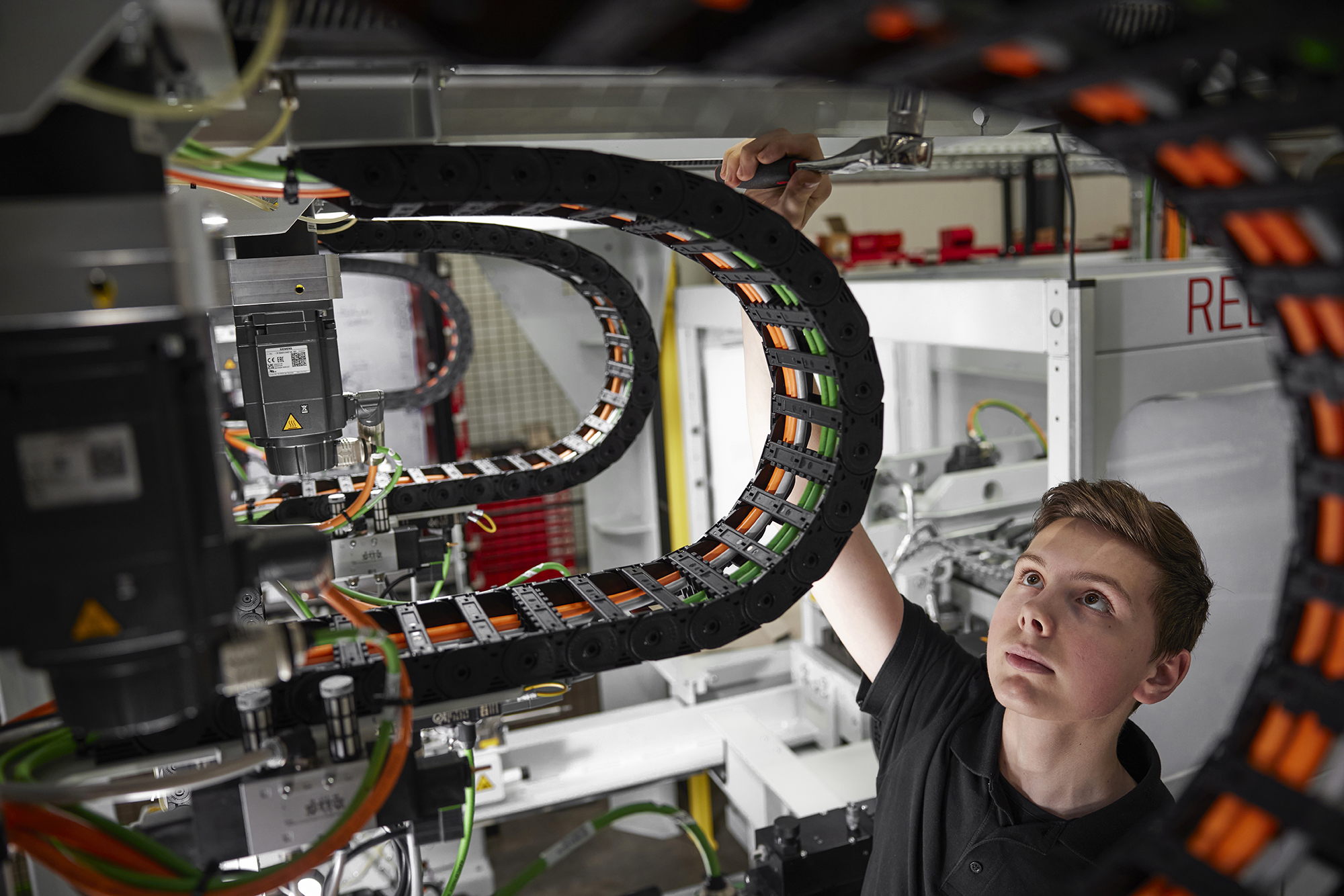 Auszubildender Mechatroniker prüft Kabelsystem und Komponenten an automatisierter Maschine.