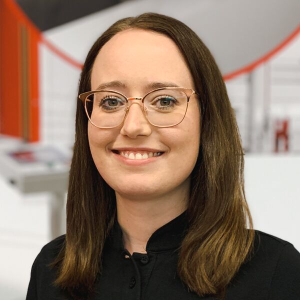 Mitarbeiterin mit Brille und dunklem Oberteil vor roter Industrieanlage.