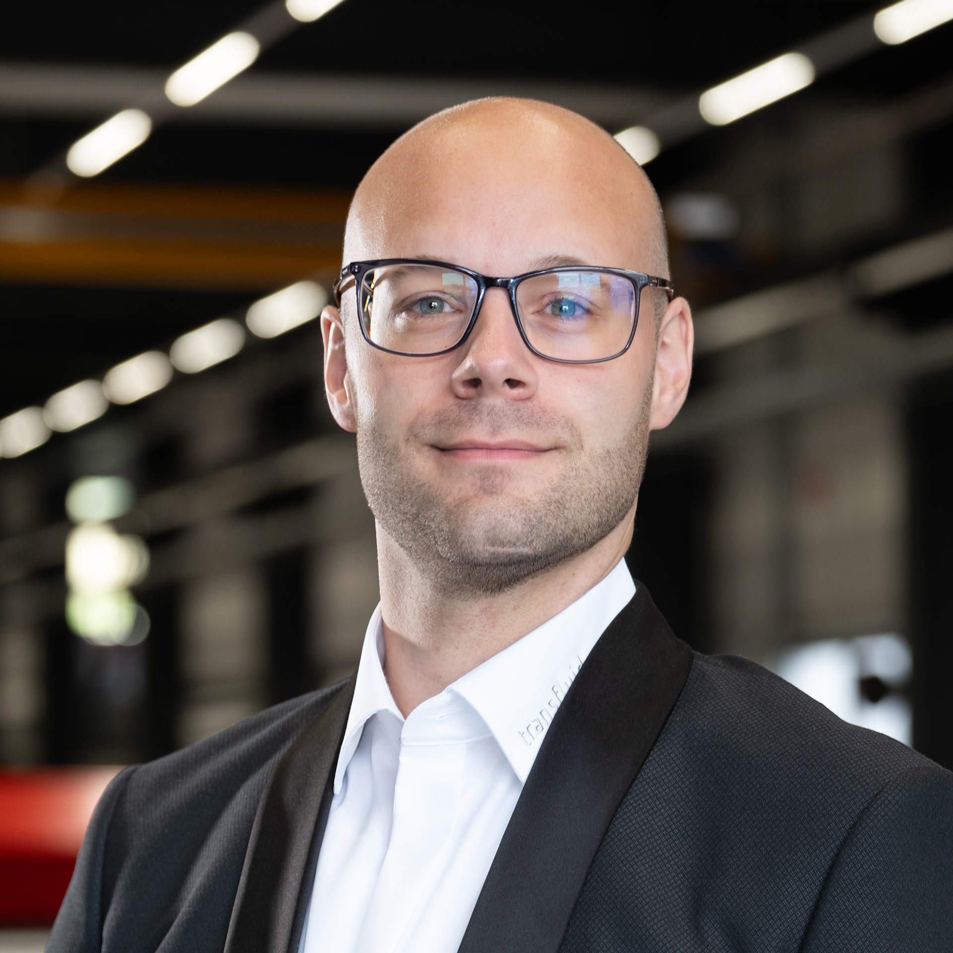 Mitarbeiter mit Brille im Anzug in moderner Industriehalle.