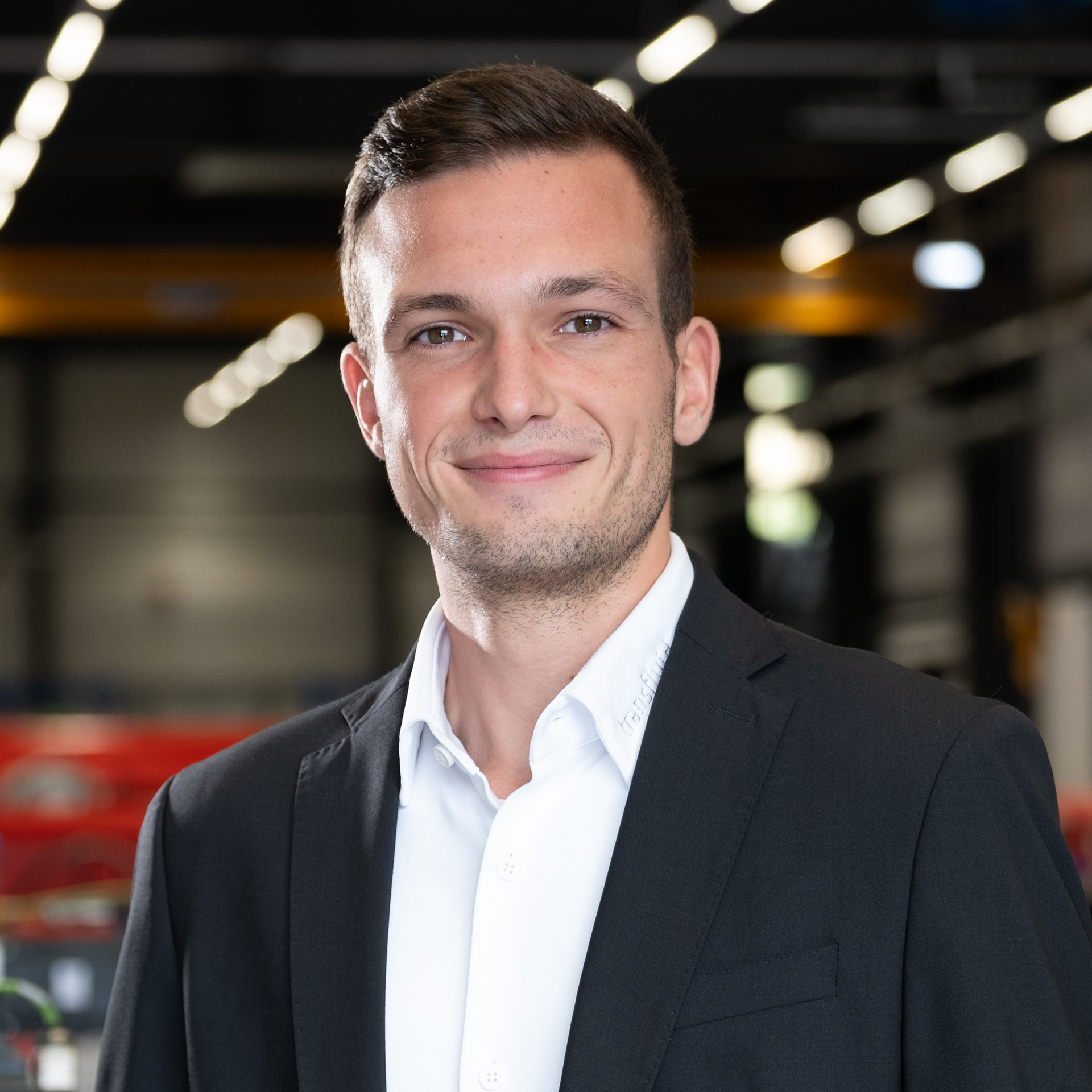 Mitarbeiter im dunklen Sakko in moderner Industriehalle mit unscharfem Maschinenhintergrund.