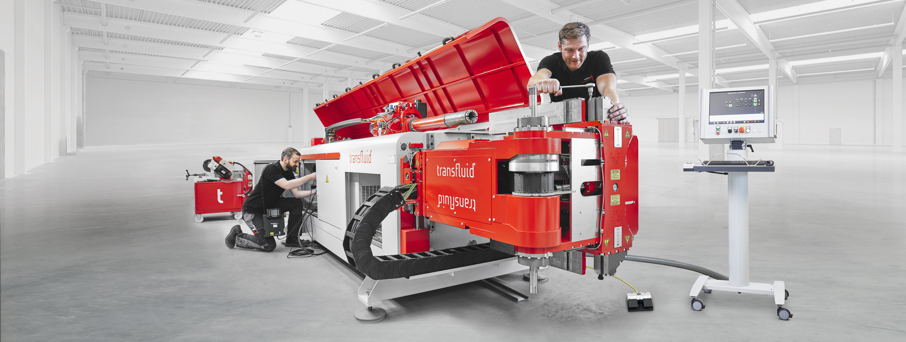 Transfluid CNC Rohrbiegemaschine mit Bedienpanel und Mitarbeitern in moderner Produktionshalle.
